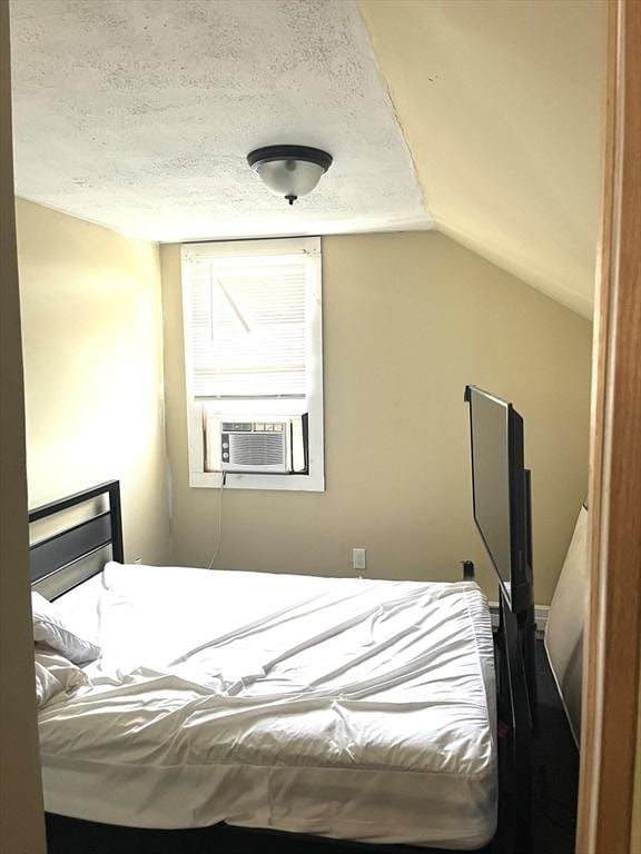 bedroom featuring cooling unit, vaulted ceiling, and a textured ceiling