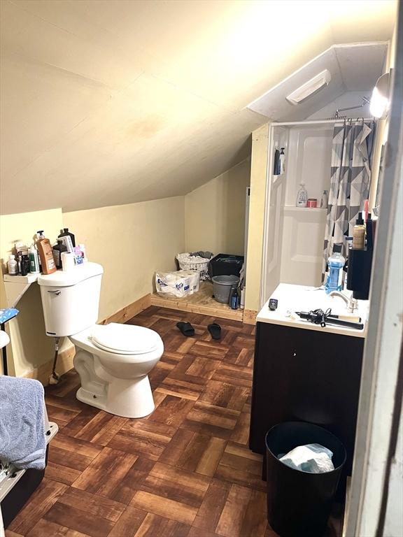 bathroom with vanity, toilet, walk in shower, parquet floors, and vaulted ceiling