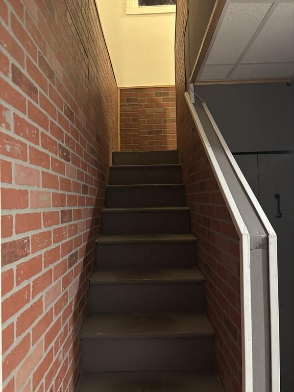 stairway featuring a paneled ceiling and brick wall