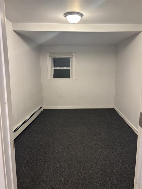 carpeted spare room featuring a baseboard heating unit