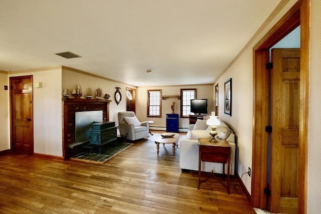 living room with wood finished floors, crown molding, visible vents, and a baseboard heating unit