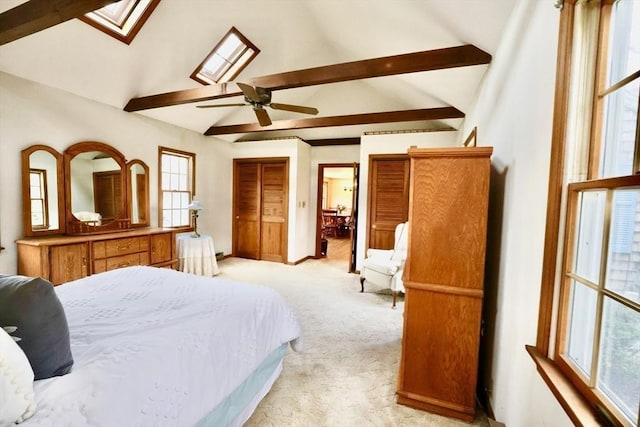 bedroom featuring a skylight, beamed ceiling, light carpet, baseboards, and a ceiling fan