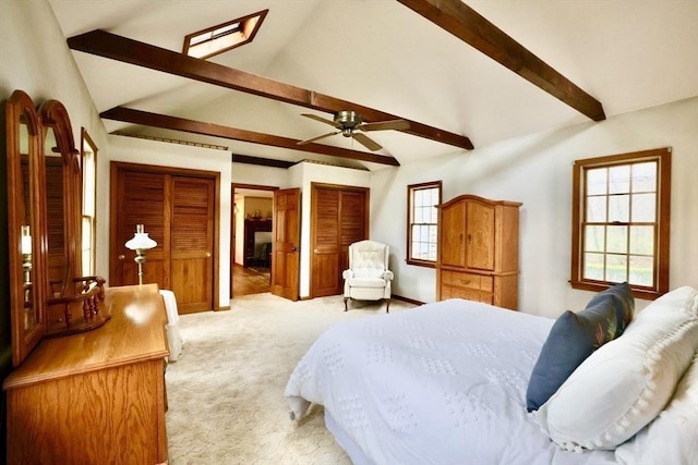 bedroom with a ceiling fan, vaulted ceiling with beams, light carpet, and multiple closets