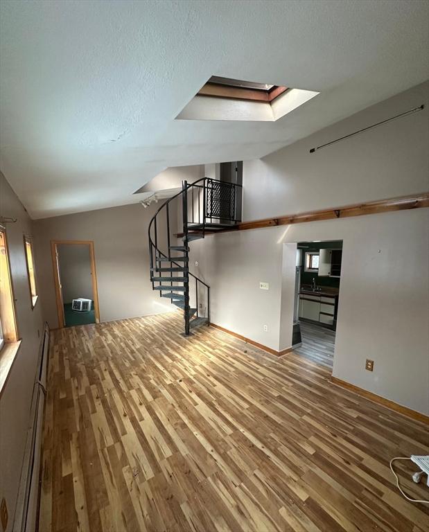 interior space with sink, a baseboard heating unit, vaulted ceiling with skylight, wood-type flooring, and a textured ceiling