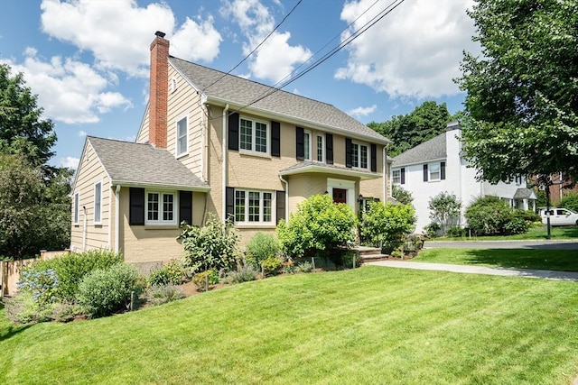 colonial-style house featuring brick siding, a front yard, roof with shingles, and a chimney