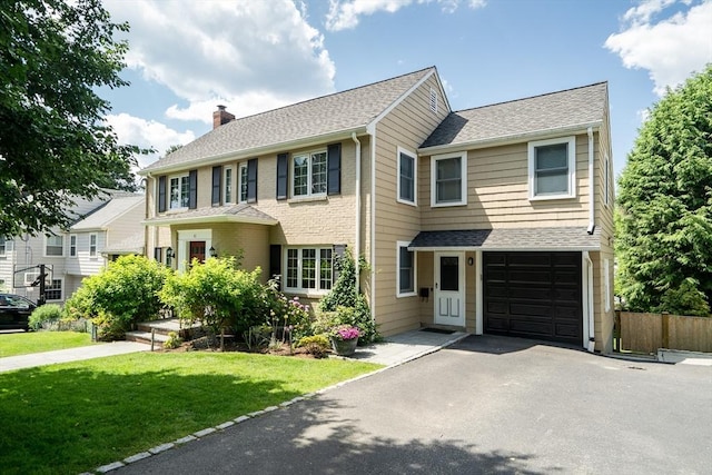 colonial-style house with driveway, a front lawn, fence, an attached garage, and a chimney