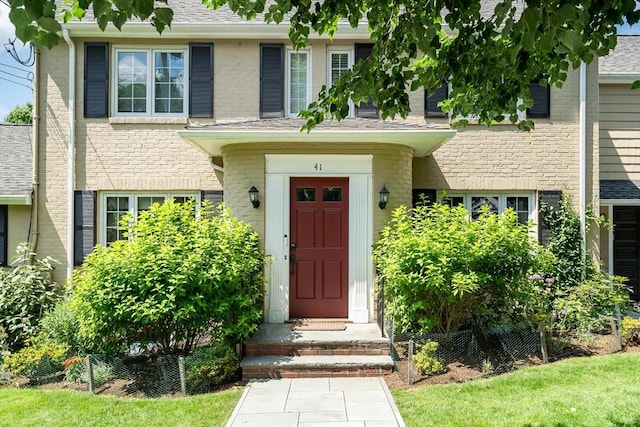 view of exterior entry featuring brick siding and roof with shingles