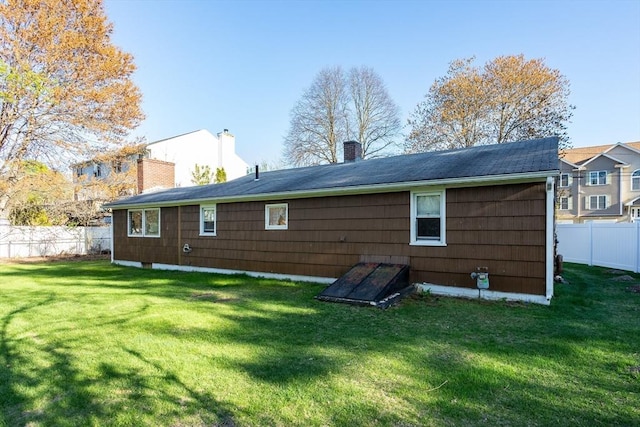 back of house with fence, a yard, and a chimney