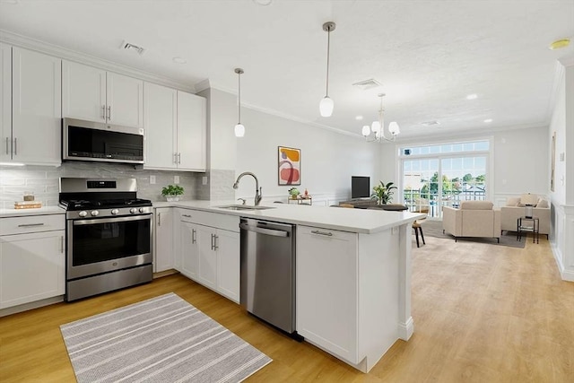 kitchen with crown molding, a peninsula, open floor plan, a sink, and appliances with stainless steel finishes