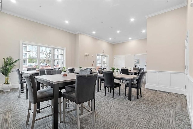 dining room featuring crown molding, a wainscoted wall, light carpet, a decorative wall, and recessed lighting