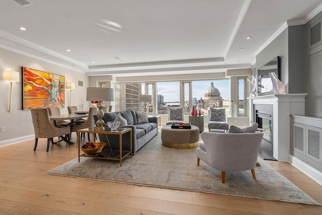 living area with a tray ceiling, hardwood / wood-style floors, a glass covered fireplace, and crown molding