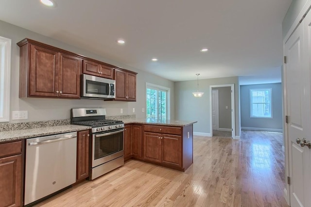 kitchen featuring kitchen peninsula, light stone counters, stainless steel appliances, light hardwood / wood-style floors, and hanging light fixtures