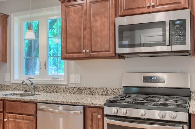 kitchen with light stone counters, sink, pendant lighting, and appliances with stainless steel finishes