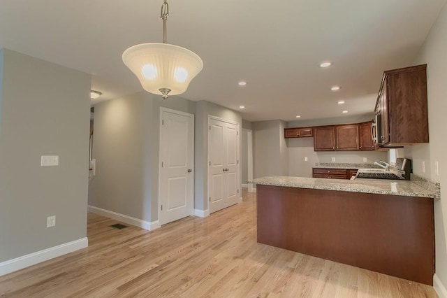 kitchen featuring light stone countertops, sink, kitchen peninsula, decorative light fixtures, and light wood-type flooring