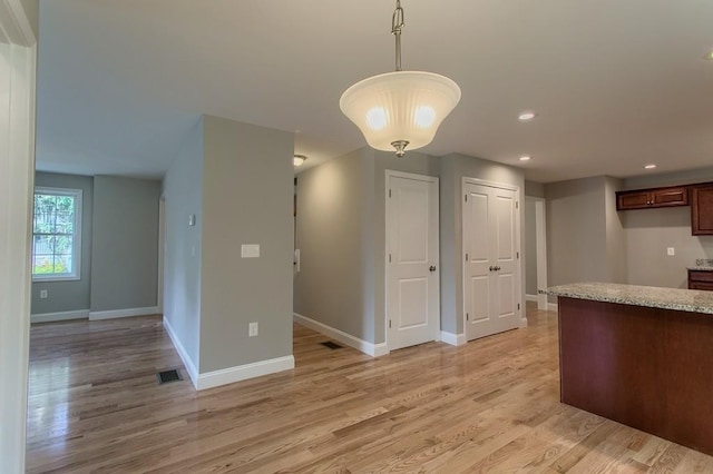 kitchen featuring decorative light fixtures, light hardwood / wood-style floors, and light stone counters