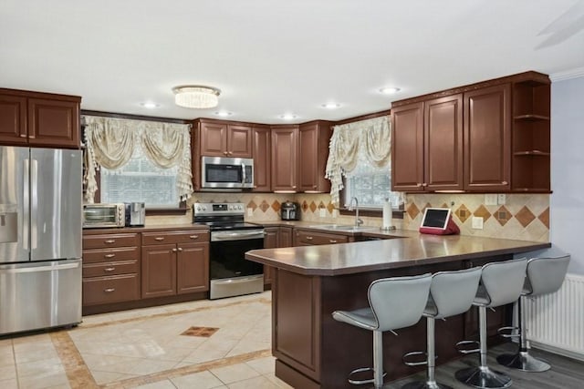 kitchen with appliances with stainless steel finishes, radiator heating unit, sink, kitchen peninsula, and a breakfast bar