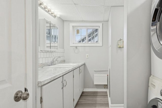 bathroom with vanity, a drop ceiling, decorative backsplash, hardwood / wood-style flooring, and stacked washing maching and dryer