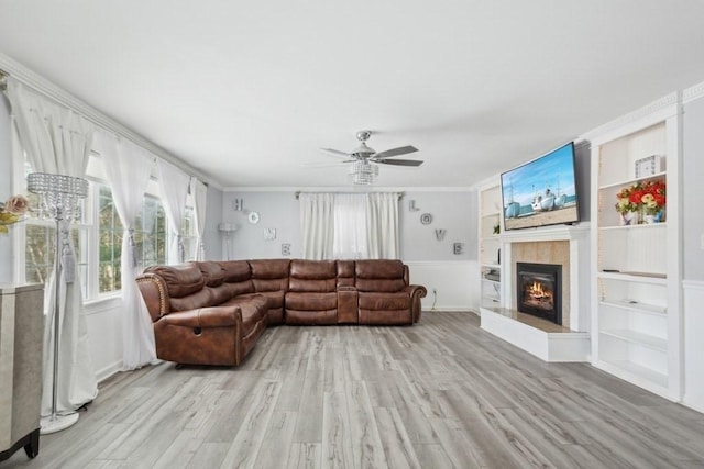 living room featuring ceiling fan, a tile fireplace, light hardwood / wood-style floors, crown molding, and built in features