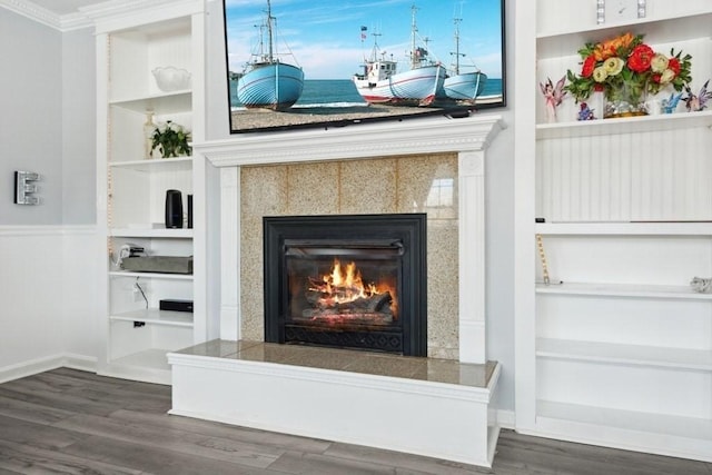 interior details featuring wood-type flooring, built in shelves, a tile fireplace, and ornamental molding