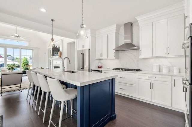 kitchen with high quality fridge, pendant lighting, sink, a kitchen island with sink, and wall chimney exhaust hood