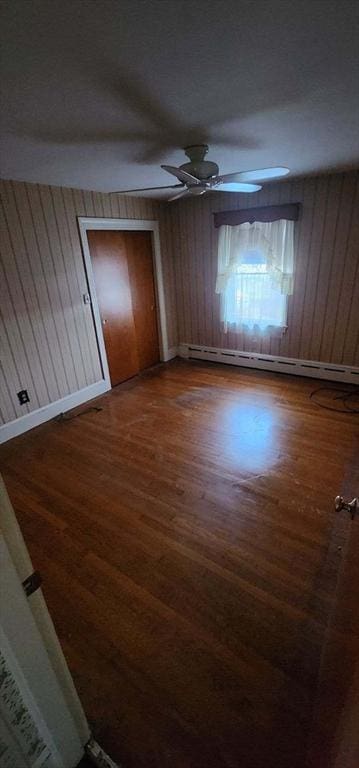 unfurnished bedroom with ceiling fan, a baseboard radiator, wooden walls, a closet, and hardwood / wood-style flooring