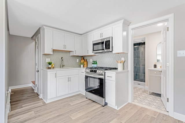 kitchen with white cabinets, light hardwood / wood-style floors, stainless steel appliances, and sink