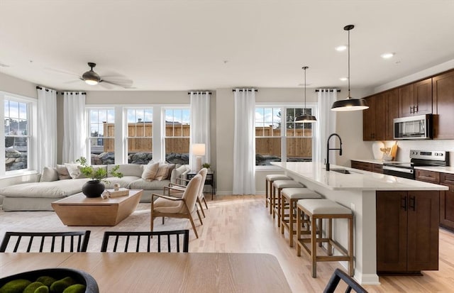 kitchen featuring an island with sink, light wood-type flooring, a sink, stainless steel appliances, and a breakfast bar area