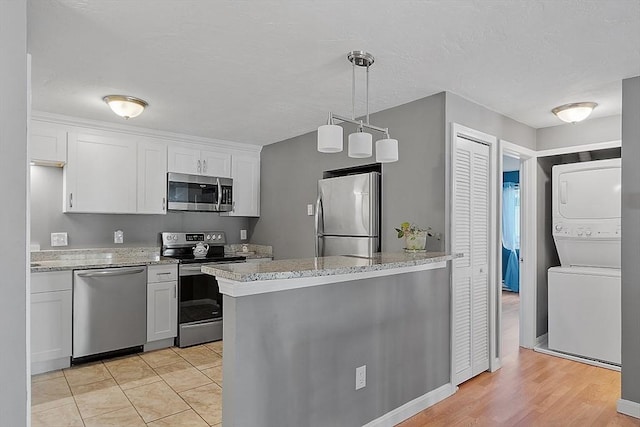 kitchen featuring stainless steel appliances, white cabinets, light stone counters, and stacked washing maching and dryer