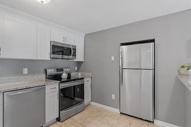 kitchen with light stone counters, light tile patterned flooring, stainless steel appliances, baseboards, and white cabinets