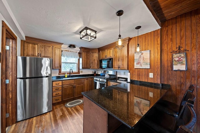 18 Marshfield Ave, Scituate, MA 02066 - kitchen with stainless steel appliances, a peninsula, brown cabinetry, a sink, and wood walls