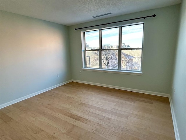 empty room featuring baseboards, a textured ceiling, visible vents, and light wood-style floors