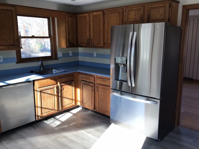 kitchen with decorative backsplash, appliances with stainless steel finishes, light hardwood / wood-style floors, and sink