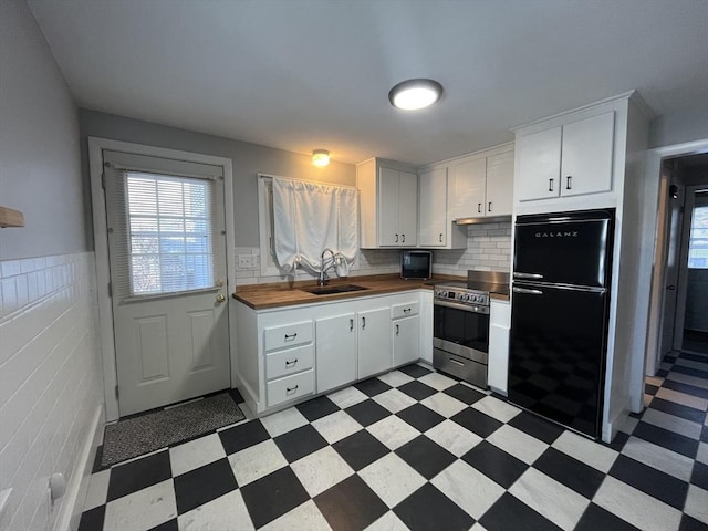 kitchen with sink, wooden counters, stainless steel range with electric stovetop, black refrigerator, and white cabinets