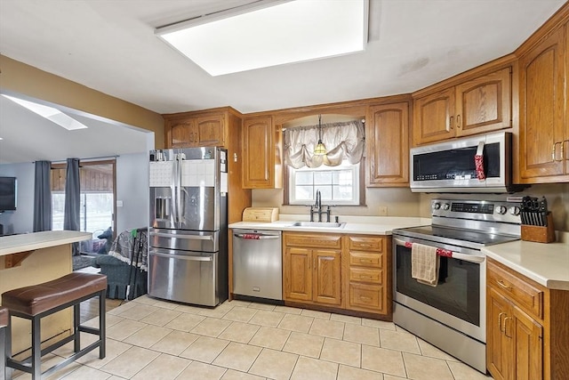 kitchen featuring stainless steel appliances, sink, light tile patterned floors, and a skylight