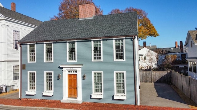 colonial inspired home featuring a chimney, roof with shingles, and fence