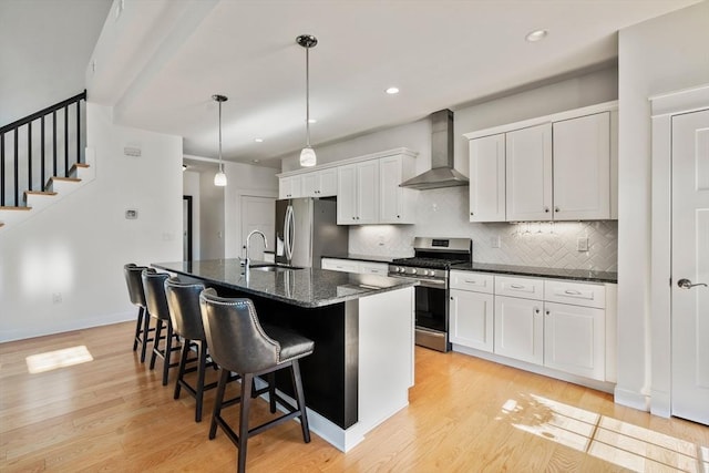 kitchen featuring a kitchen island with sink, a kitchen breakfast bar, wall chimney exhaust hood, a sink, and appliances with stainless steel finishes