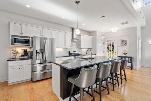 kitchen with appliances with stainless steel finishes, a sink, wall chimney exhaust hood, decorative backsplash, and visible vents