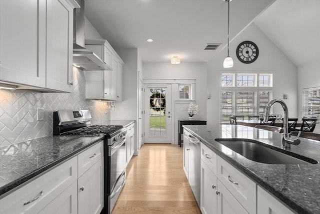 kitchen with visible vents, wall chimney range hood, light wood-type flooring, a sink, and appliances with stainless steel finishes