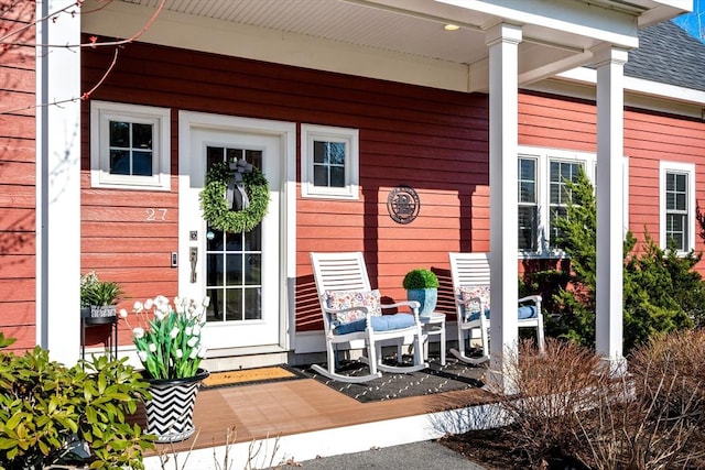view of exterior entry with a porch and roof with shingles