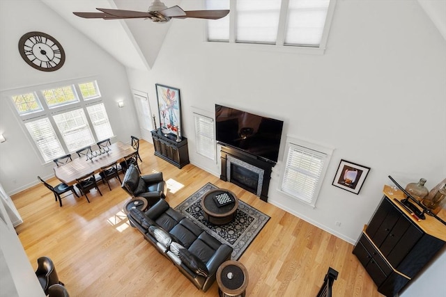 living room with light wood-style floors, high vaulted ceiling, baseboards, and a ceiling fan