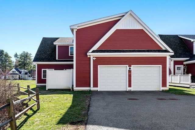 traditional-style house with board and batten siding, driveway, a front yard, fence, and a shingled roof