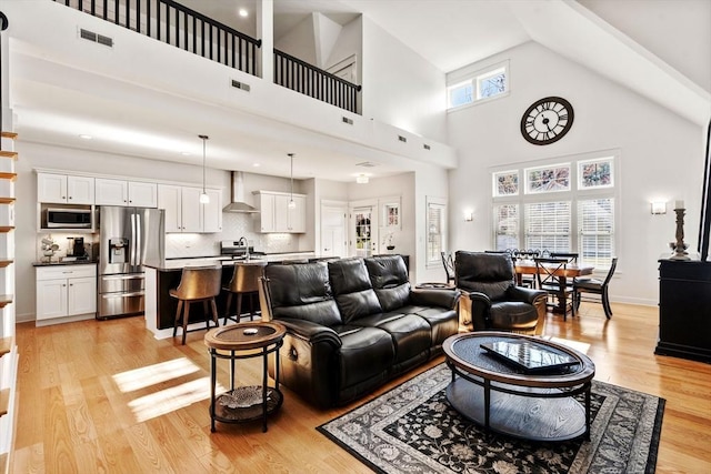 living room featuring a high ceiling, light wood-style flooring, and visible vents