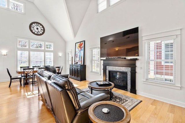 living area featuring high vaulted ceiling, a glass covered fireplace, baseboards, and light wood finished floors