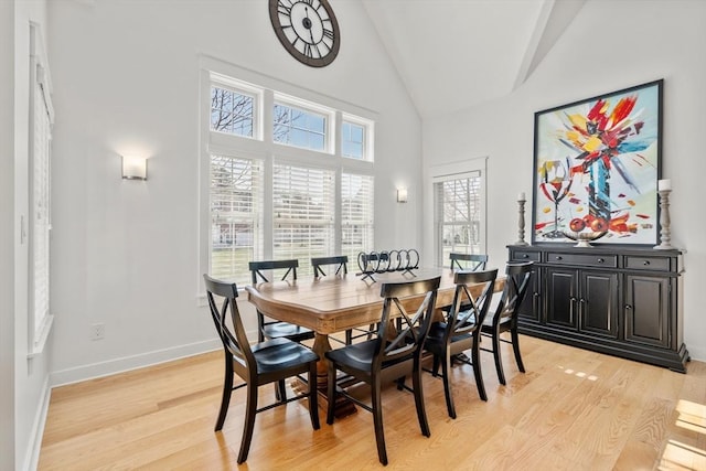 dining room featuring baseboards, high vaulted ceiling, and light wood-style flooring
