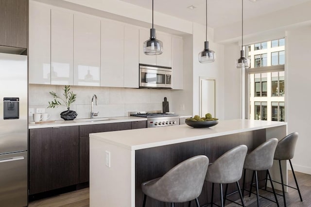 kitchen with appliances with stainless steel finishes, wood finished floors, light countertops, a kitchen island, and modern cabinets