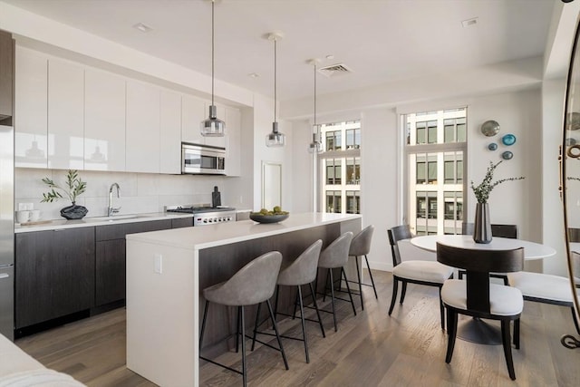 kitchen featuring stainless steel appliances, modern cabinets, light countertops, a breakfast bar, and a kitchen island