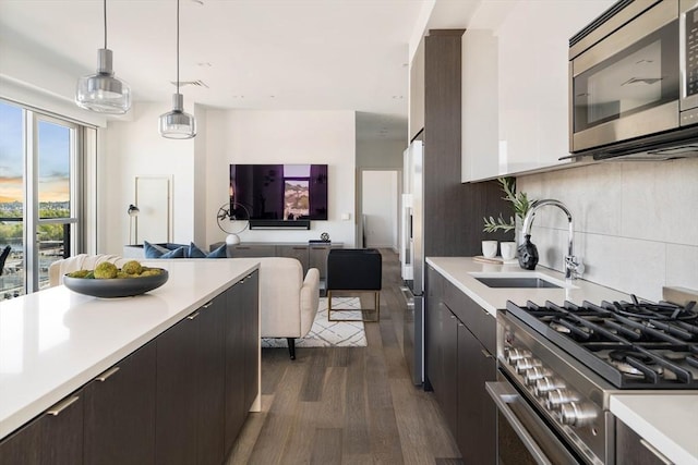 kitchen with stainless steel appliances, light countertops, open floor plan, a sink, and dark wood-style flooring