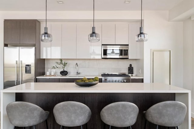 kitchen featuring appliances with stainless steel finishes, a sink, light countertops, white cabinets, and a kitchen bar