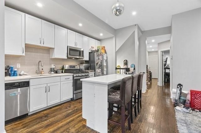 kitchen with appliances with stainless steel finishes, a sink, dark wood-style flooring, light countertops, and a breakfast bar