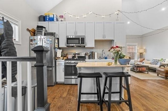 kitchen with stainless steel appliances, vaulted ceiling, light countertops, a breakfast bar area, and wood finished floors